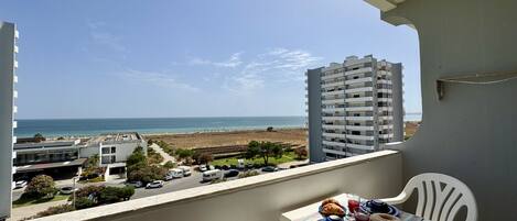 Un balcón con una mesa lista para el desayuno, con vista a una playa y un estacionamiento con vehículos.