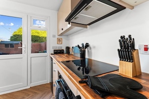 A modern kitchen with a wooden countertop, a built-in stove, and a window overlooking a garden.