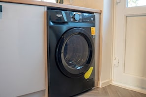 A black front-loading washing machine with a control panel, placed in a room with a wooden floor and a white door.