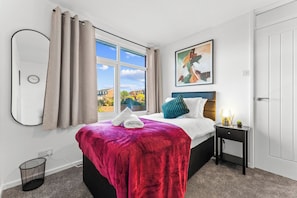 A hotel room with a bed, a bedside table, a window with curtains, a wall clock, and a painting.