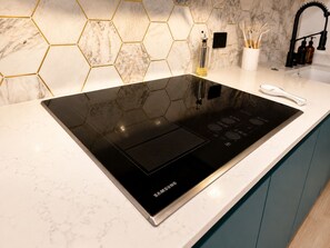 Ett modernt kök med en svart induktionshäll från Samsung, en marmorbeklädd vägg bakom spisen med hexagonala mönster och en vit bänkskiva.
