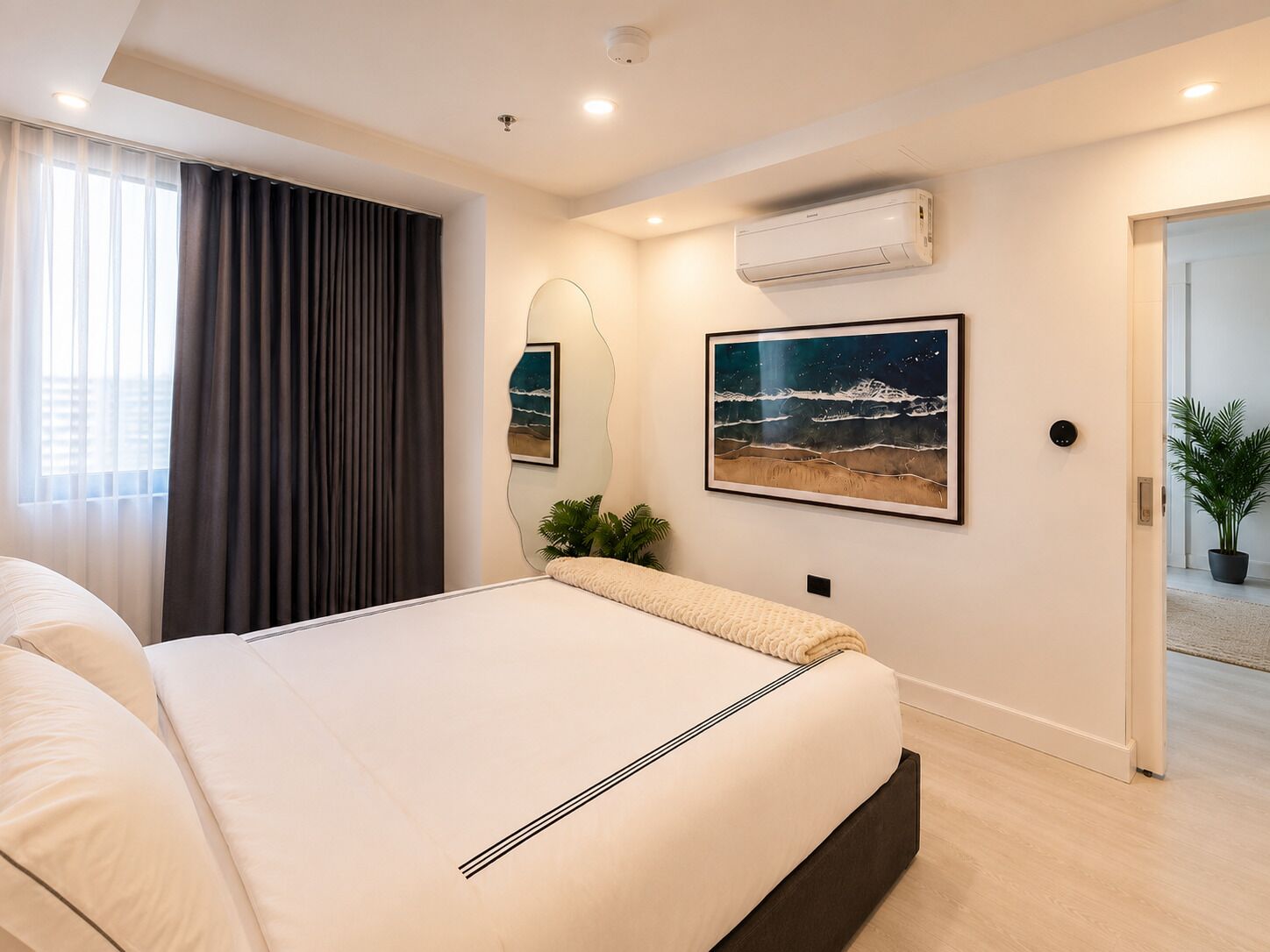 Ein modernes Schlafzimmer mit einem großen Bett, einer Wand-Klimaanlage und zwei gerahmten Bildern.