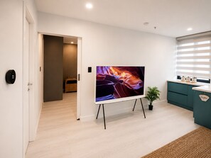 Ett modernt vardagsrum med en platt-TV på ett TV-bord, en plats för att göra kaffe och en dörr som leder till ett annat rum.