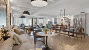 Ein modernes Wohnzimmer mit einer Couch, einem runden Esstisch und einer Küchenzeile inklusive Kühlschrank und Schränken.