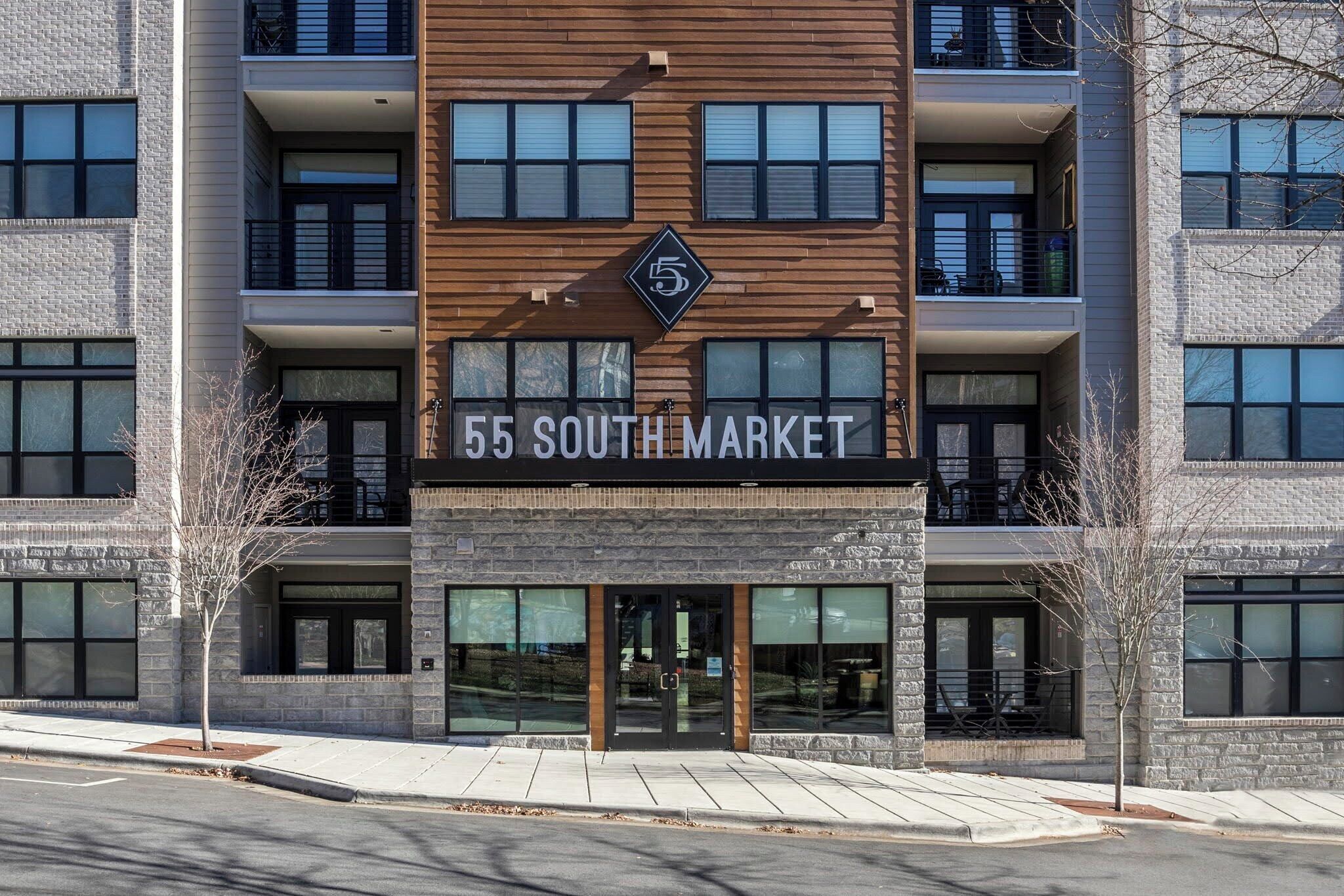 En byggnad med flera våningar, ett stort och väl synligt skylt med texten ”55 SOUTH MARKET”, stora fönster och en fasad av sten.