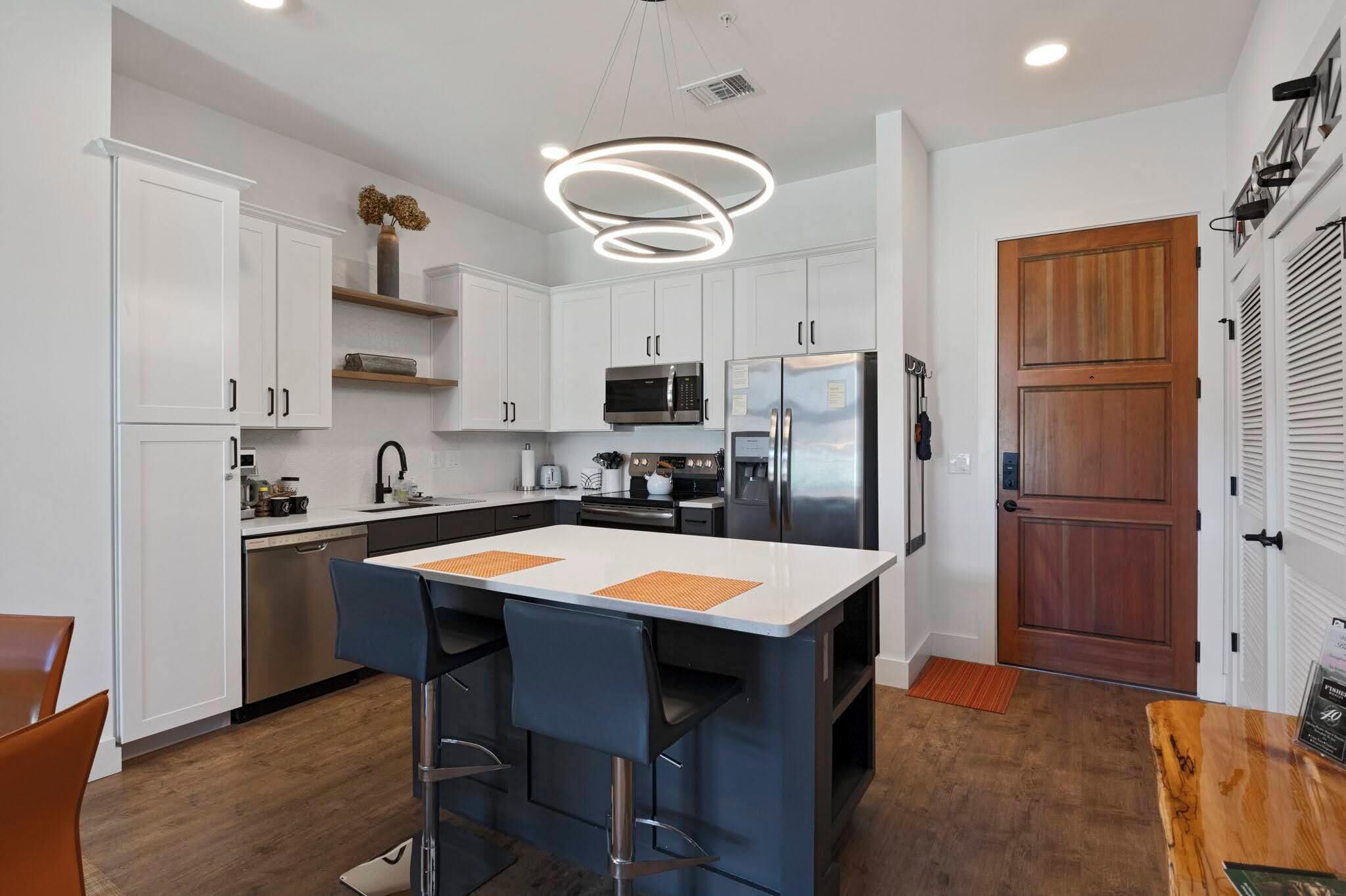 A modern kitchen with white cabinets, stainless steel appliances, and a central island with bar stools.
