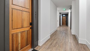 Ein Flur mit einer Holztür links, weißen Wänden und einem Holzboden.