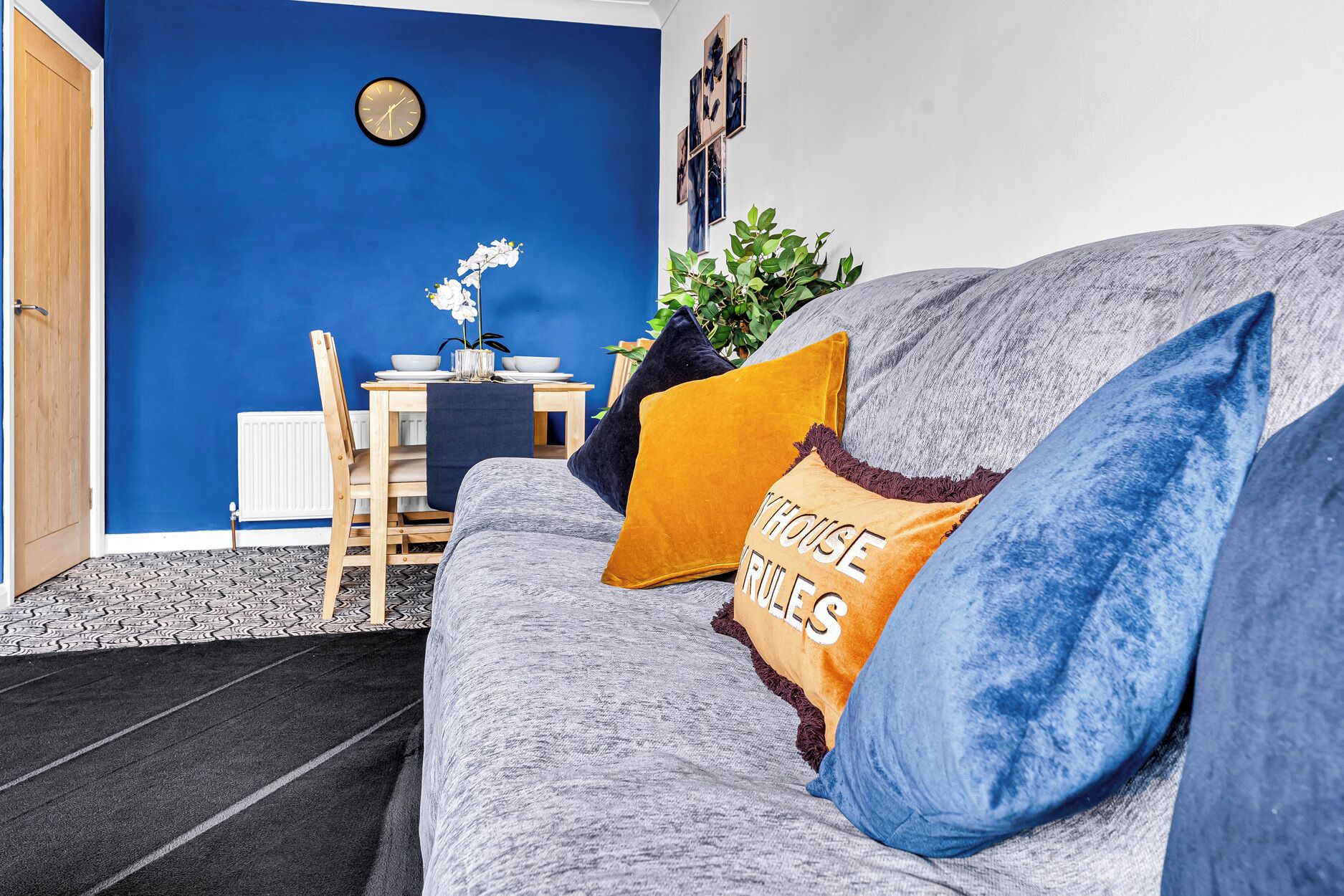 Ein Wohnzimmer mit blauer Wand, einem grauen Sofa und einem Esstisch mit Stühlen.