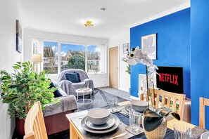 Ein modernes Wohnzimmer mit Essbereich, großen Fenstern, einer blauen Akzentwand und einem Netflix-Schild.