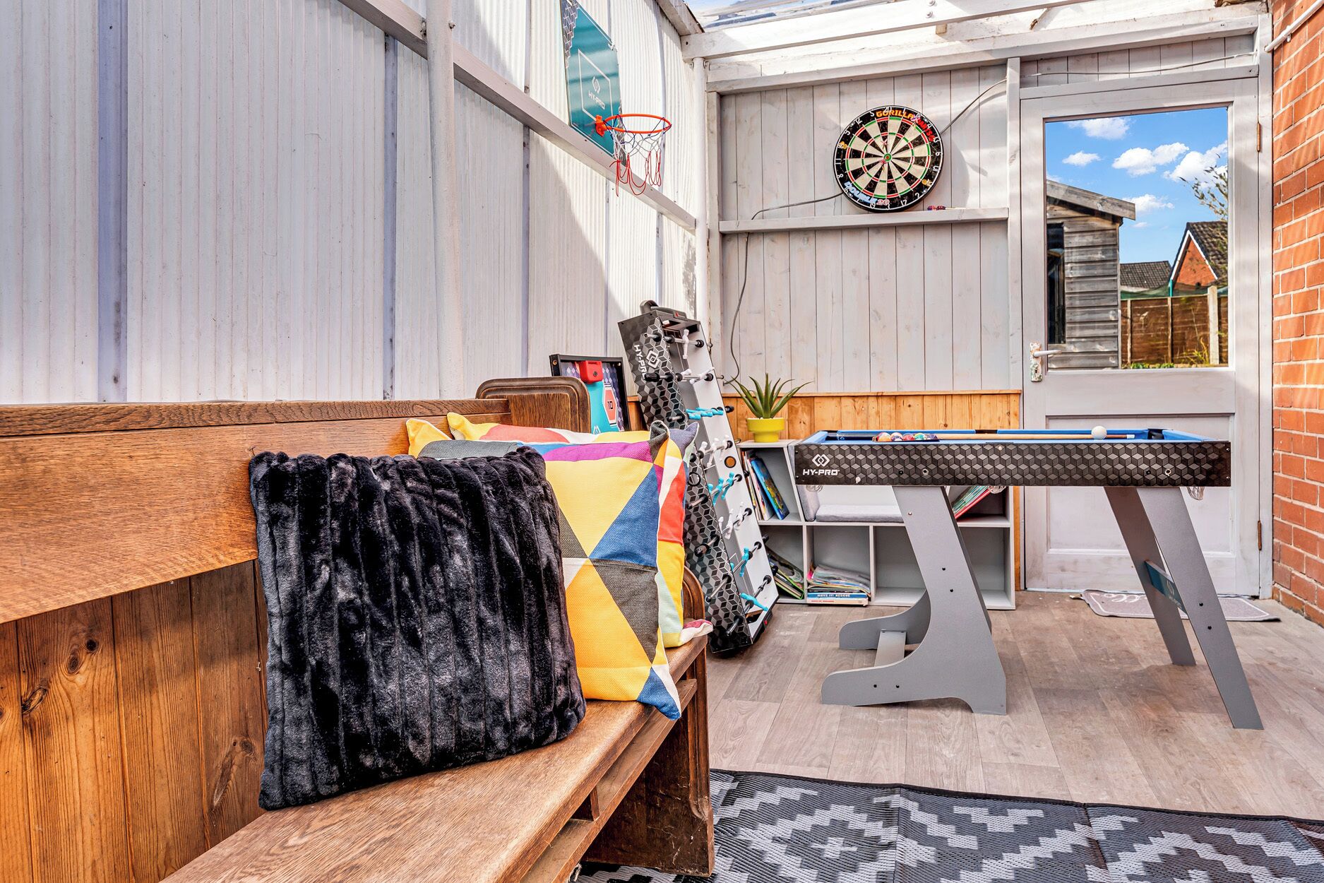 Un espace extérieur accueillant avec un banc en bois, un jeu de fléchettes et une table de billard.