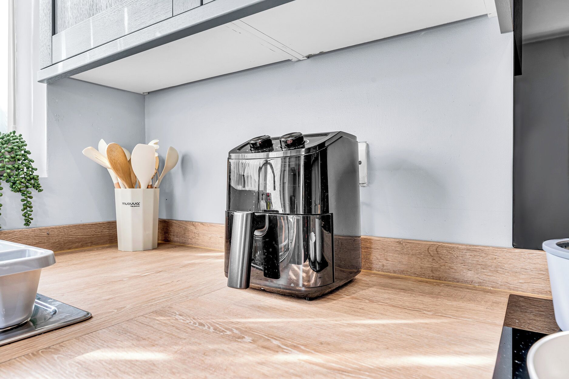 Una cocina con una cafetera de acero inoxidable, utensilios de madera en un recipiente y una planta.