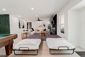 A modern living room with a pool table, two beds, a sofa, a coffee table, and a fireplace.