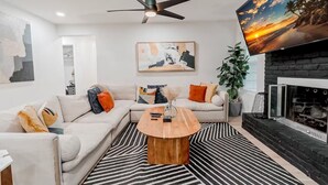 A modern living room with a sectional sofa, a coffee table, a fireplace, and a painting of a beach scene.