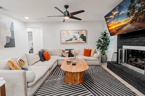 A modern living room with a sectional sofa, a coffee table, a fireplace, and a painting of a beach scene.