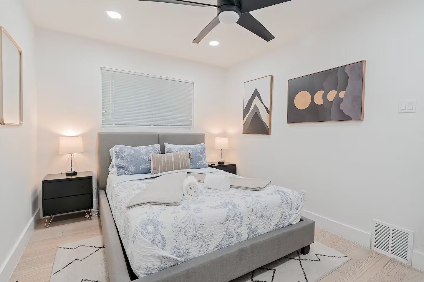 A bedroom with a bed, two bedside tables, a ceiling fan, and artwork on the walls.