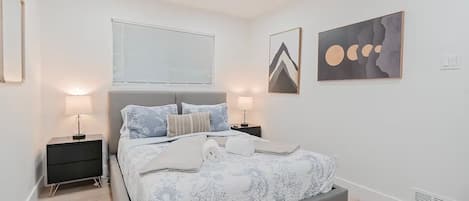 A bedroom with a bed, two bedside tables, a ceiling fan, and artwork on the walls.