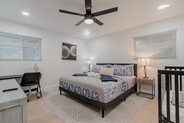 A bedroom with a bed, bedside tables, a desk, a chair, a ceiling fan, and a window with blinds.