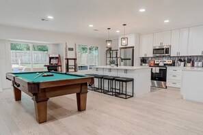 A modern kitchen with a pool table, bar stools, and a microwave.