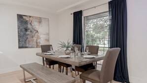 A dining area with a rectangular table set for four, flanked by two chairs, a bench, and a large window with dark curtains.