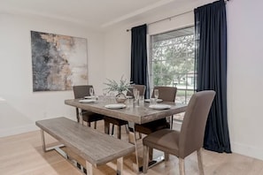 A dining area with a rectangular table set for four, flanked by two chairs, a bench, and a large window with dark curtains.