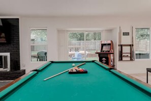 A pool table with a cue stick and balls, a fireplace, and a basketball arcade game.