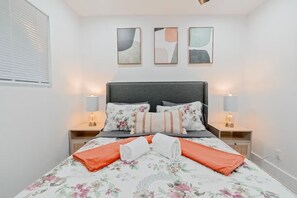 Una cama bien hecha con ropa de cama floral, dos lámparas de noche y arte abstracto en la pared.