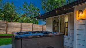 A hot tub outside a house with a wooden fence and string lights in the background.