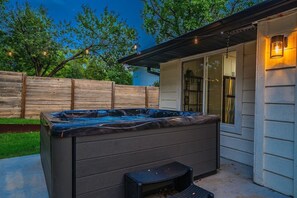 A hot tub outside a house with a wooden fence and string lights in the background.