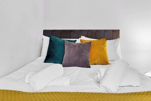 A bed with a headboard, white bedding, and three pillows in different colors. - Stoke Townhouse (Stoke-on-Trent)