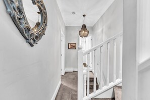 A hallway with a white railing, a chandelier, and a framed picture on the wall. - Stoke Townhouse (Stoke-on-Trent)