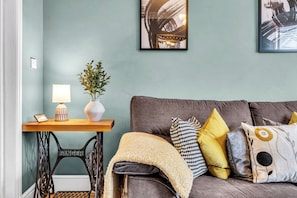 A room with a sewing machine, a table with a lamp and a vase, and a sofa with patterned cushions. - Stoke Townhouse (Stoke-on-Trent)