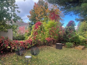 Um jardim com gramado, duas cadeiras e um edifício vermelho ao fundo.