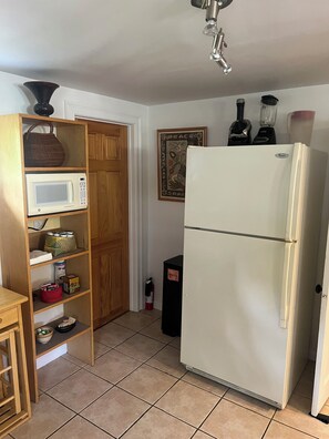 Eine Küche mit Mikrowelle, Kühlschrank, Holzschrank, Feuerlöscher und einem an der Wand befestigten Mixer.