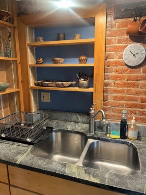 A kitchen with two stainless steel sinks, wooden shelves with decorative bowls, a basket, and a clock on the wall. - Beautifully renovated 2-bedroom/1 bath apt. Parking and Laundry on site. (Burlington)