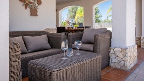 A wicker sofa set with a table and wine glasses, a stone pillar, and a wall-mounted flower decoration.