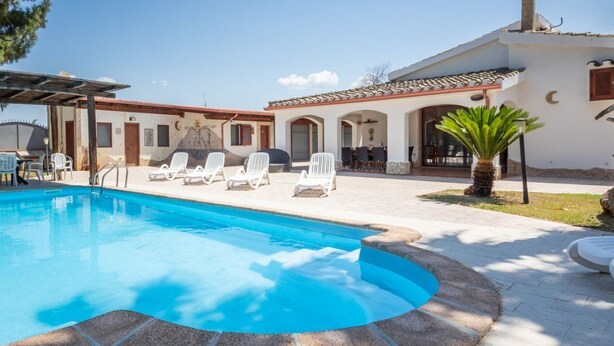 A swimming pool with lounge chairs, a barbecue area, and a covered patio.