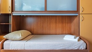 A single bed with a patterned bedspread, a pillow, and a rolled towel.