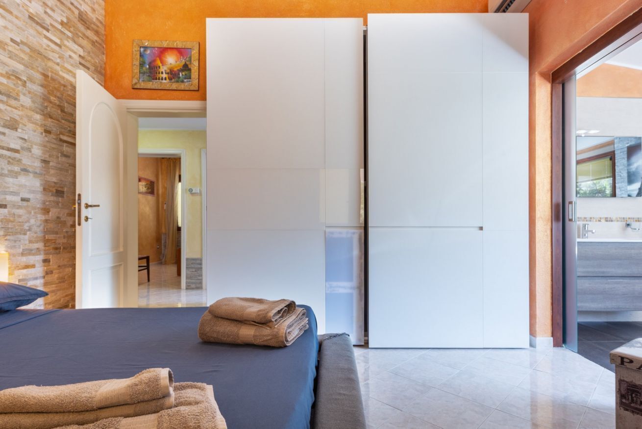Una habitación de hotel con una cama, un armario blanco, un cuadro en la pared y vistas a través de un ventanal.