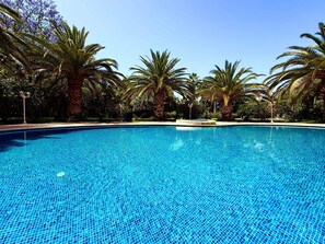 A clear blue swimming pool surrounded by palm trees and greenery. - Villa Amazura 6 Bedroom With Private Pool (Marrakech)
