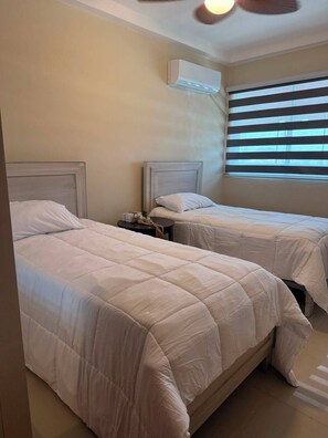 Een hotelkamer met twee bedden, een plafondventilator en een raam met zonwering.