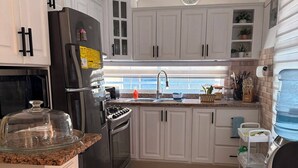 A modern kitchen with white cabinets, a stainless steel refrigerator, a stove, and a sink. - Deluxe Unique 2BR/2BA Apartment – Stylish, Modern at San Cristobal City, DR. (San Cristóbal)