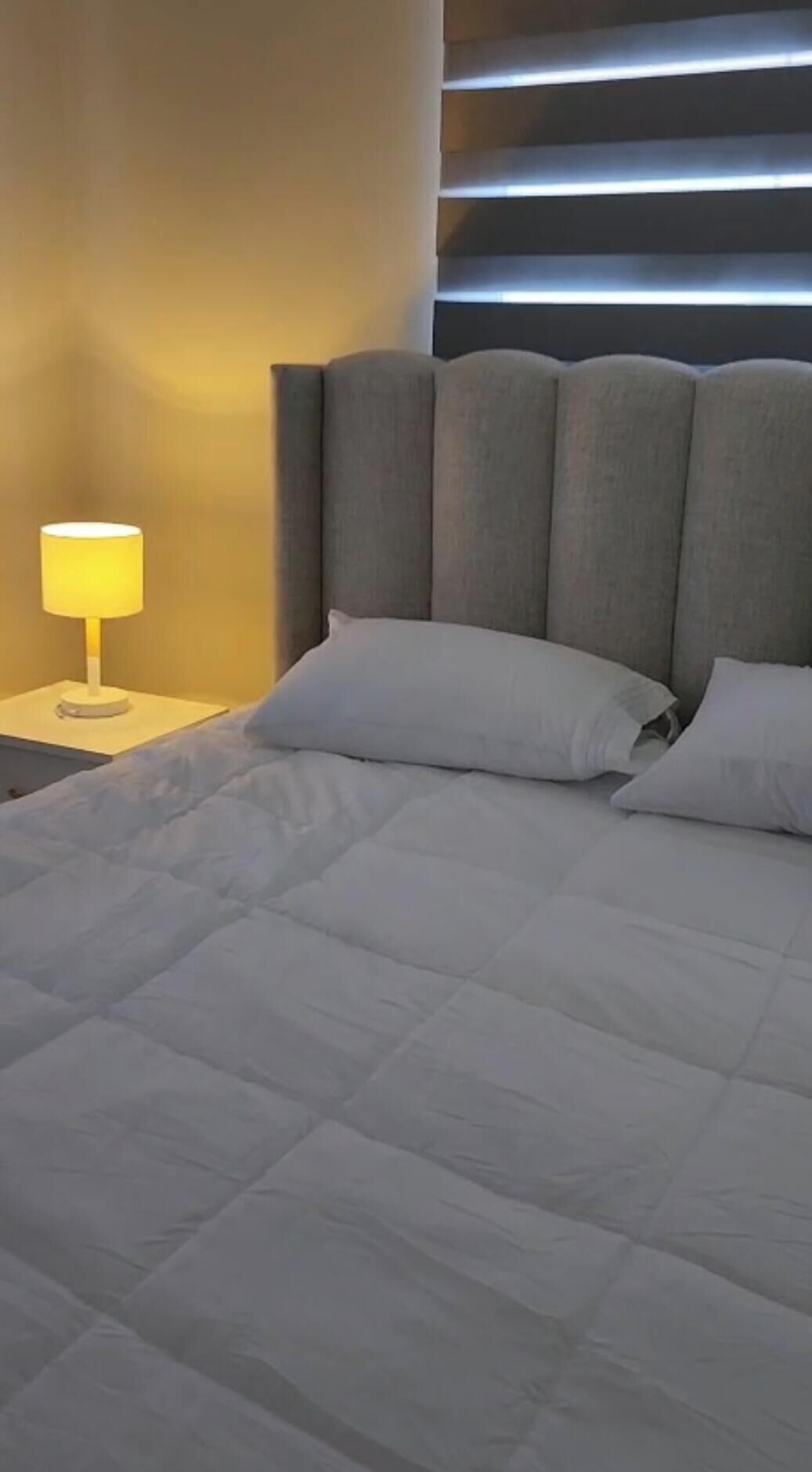 Uma cama com cabeceira, abajur e almofadas.