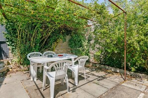 Eine Terrasse im Freien mit Tisch und Stühlen, umgeben von Pflanzen und einer Steinmauer.