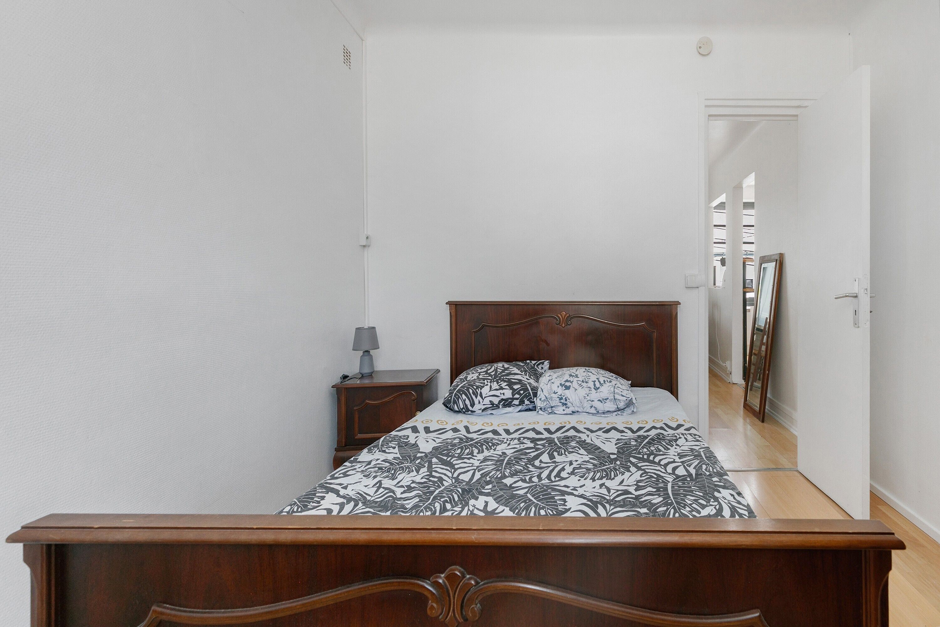 Un dormitorio con una cama de madera, una mesita de noche, una lámpara y un espejo en la pared.