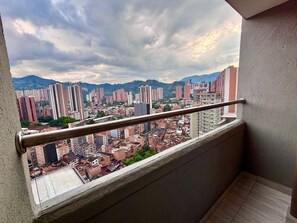Ein Balkon mit Metallgeländer, der auf einen Stadtblick mit verschiedenen Gebäuden und einem Berg im Hintergrund zeigt.