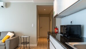 A compact kitchen with a microwave, stove, and sink. There's a small round table with a chair, a sofa with cushions, and a fire extinguisher mounted on the wall. - Cantinho da Fonte Apartment with Mountain View, Wi-Fi, and Air Conditioning (Agua de Pau)