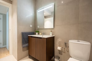 Een moderne badkamer met een houten wastafelmeubel, een grote spiegel, een toilet en een handdoek aan een rek.