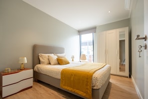 Een slaapkamer met een bed, nachtkastje, lamp en een kledingkast.