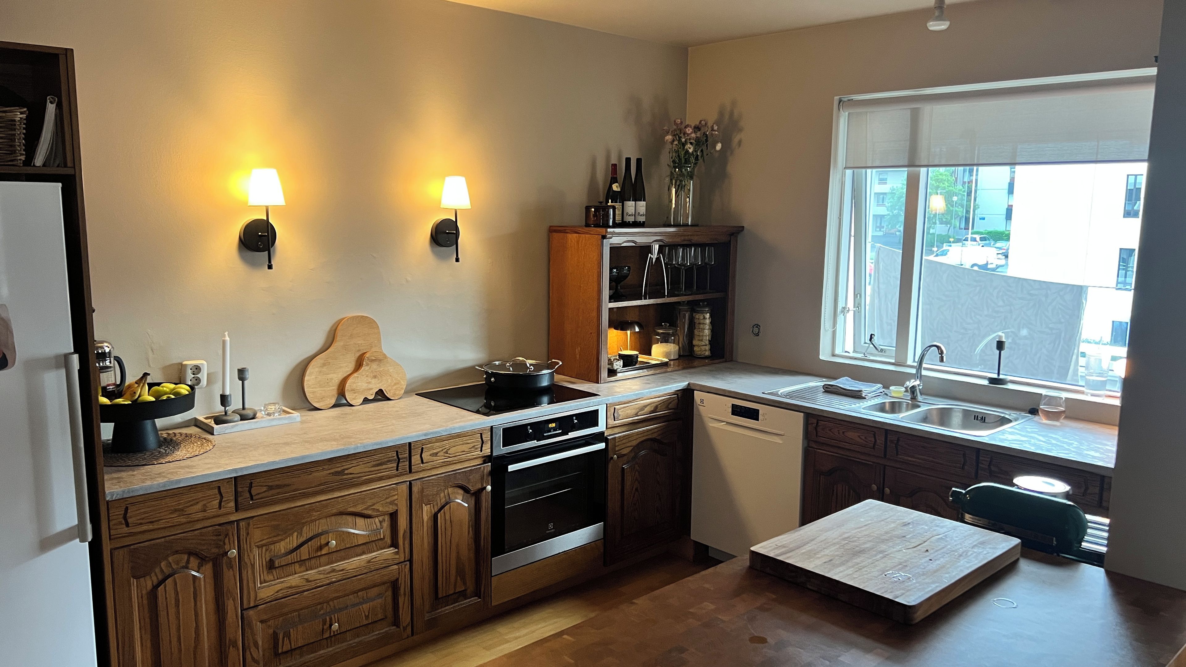 Une cuisine moderne avec des meubles en bois, un four encastré, un lave-vaisselle et une fenêtre donnant sur la rue.