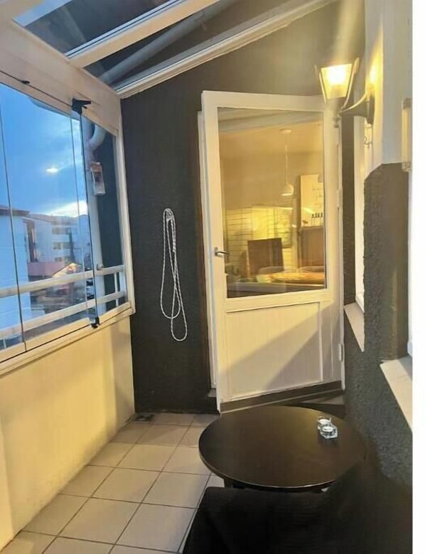 A small balcony with a glass door leading to a room, a round table, and a hanging light fixture.